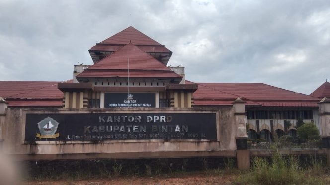 
					Kantor DPRD Kabupaten Bintan dari sisi depan plang nama telah rusak serta dipenuhi rumput liar